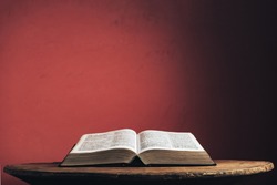 Open Holy Bible on a old brown round wooden table. Beautiful red wall background.
