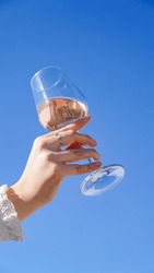 woman hands holding a glass of rosé wine in the air, hand in the blue sky