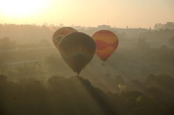 Three hot air balloons flying over the trees at sunrise