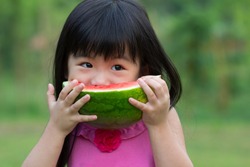 Little Asian kid with a piece of watermelon in park