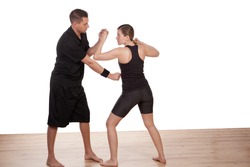 Male instructor teaching a barefoot young woman kick boxing demostrating how to block a punch and penetrate the opponents defenses