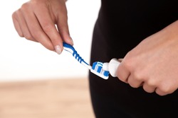 Cropped view of a woman sqeezing toothpaste from a tube onto the bristles of a plastic toothbrush