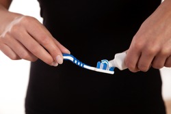 Closeup cropped view of a womans torso and hands as she sqeezes toothpaste onto a toothbrush
