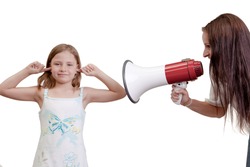 Fun humorous image of a naughty little girl playing deaf sticking her fingers in her ears while her mother shouts at her with a megaphone isolated on white