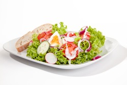 Fresh mixed leafy green salad with hard boiled egg topped with salad dressing served with a slice of bread on a white platter