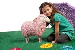 Cute pretty little girl sitting on the floor on an artificial meadow cudddling a large pink woolly toy sheep with a lovely smile on her face