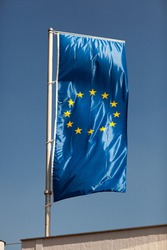 European Union flag flying from a rooftop flagpole against a blue sky