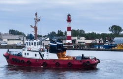 Marine tug inside the harbour. Big lighthouse at port. Latvia, Liepaja.