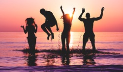 Happy friends jumping inside water on tropical beach at sunset - Group of young people having fun on summer vacation - Youth lifestyle, party and friendship concept - Focus on bodies silhouette