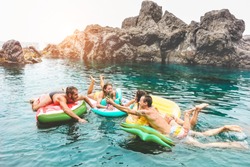 Happy friends floating with lilos, drinking beer in sea natural pool - Young trendy people having fun swimming in summer vacation - Youth lifestyle, travel and party concept - Focus on tree left guys