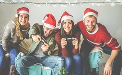 Group of happy friends having fun with video games console on christmas time - Young millennial people playing and laughing on winter holiday with vintage light on background - Focus on right man face