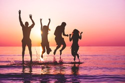 Happy friends jumping inside water on tropical beach at sunset - Group of young people having fun on summer vacation - Youth lifestyle, party and friendship concept - Focus on bodies 