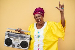 Happy senior black woman with traditional african dress dancing holding vintage stereo - Focus on face