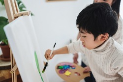 Asian kid painting on canvas during art class at home - Focus on child eye