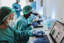 Multiracial medical scientists in hazmat suit working with microscope and laptop computer inside hospital lab - Focus african man face