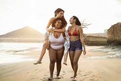 Happy multiracial women with different bodies and skins having fun in summer day on the beach - Soft focus on african girl face