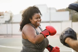 African curvy woman and personal trainer doing boxing workout session outdoor - Focus on face