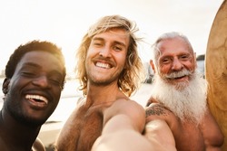 Multi generational surfer friends having fun doing selfie on the beach after surf session - Focus on center guy face