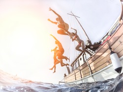 Multiracial young people diving from sailing boat into the sea - Cheerful friends having fun in summer party day - Vacation and friendship concept - Fisheye lens distortion with back lighting
