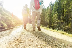 Two friends hiking in switzerland at sunrise - Young people walking in mountain trails with sun back light - Trekking and healthy vacation concept - Focus on man feet - Warm filter