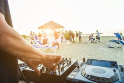 Dj mixing at sunset beach party in summer vacation - Disc jockey hands playing music for tourist people in chiringuito bar - Music and fun concept - Focus on right hand - Tilted horizon composition