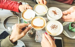 Friends group toasting cappuccino and milk with cocoa - Close up of young people drinking in coffee shop bar restaurant - Breakfast and socializing concept - Warm filter - Focus on right bottom hand