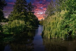 Sunset over the river Avon running through Chippenham Wiltshire. Weeping willow drooping into the water. Other broad leaf trees on grassy banks.