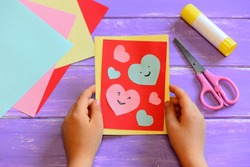 Child is holding a Valentines day card diy in his hands. Small kid made a handmade Valentines day greeting card with hearts smiles. Cute and simple paper crafts for kindergarten. Paper cutting hearts