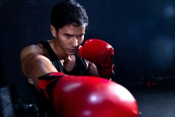 Brutal boxer fighter, confident young athlete asian man in red boxing gloves, punching a sand bag in professioal gym. Sportsman muay thai boxer work out, training, fighting in gloves.