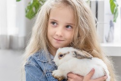 Caucasian child hold rabbit in arms, Children play with real rabbit. Laughing child at Easter egg hunt with white pet bunny. Little toddler girl playing with animal. Summer fun for kids with pets.