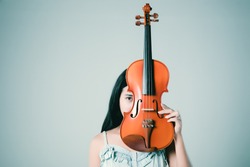 Asian woman holding violin in hand. Beautiful woman playing violin on grey background.