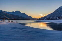 View of beautiful sunet at Lake Silvaplana, Switzerland, in cold winter evening with foreground snow and mountain range background
