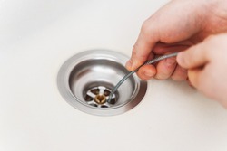 Plumber using drain snake to unclog kitchen sink.