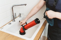 Plumber unclogging kitchen sink with professional force pump cleaner.
