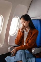 Female asian chinese japanese people passenger experiencing airsickness, clenching sick bag and looking uneasy mid-air.
