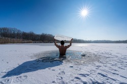 Young man holding an ice floe above his head while taking an ice bath