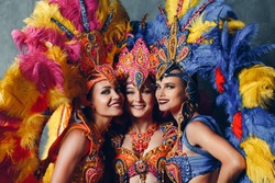 Three Women smiling portrait in brazilian samba carnival costume with colorful feathers plumage.