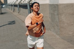 Young indian woman runner jogging in wet sweaty t-shirt at city street.