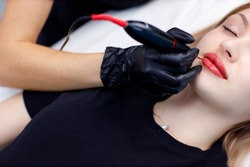 Cosmetologist applying pink pigment permanent tattoo on female lips with tatooing needle machine