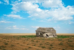 Abandoned Wooden Collapsed Barn in Rural Farmland with Dirt and Patches of Grass with Puffy Clouds in Blue Sky