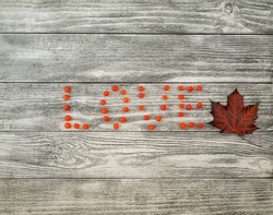The word love is written with rowan berries and maple leaf on wooden background, top view, copy space