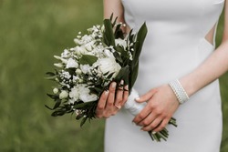 The bride is holding a beautiful wedding bouquet of white flowers. White evening dress, beautiful jewelry on the hand