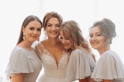 Portrait of the bride with her friends. The bride in a voluminous white dress and her beautiful friends in white evening dresses are posing. Brunettes. Open shoulders. Morning of the bride.