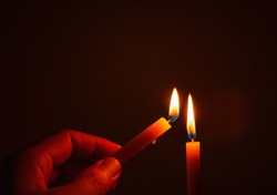 
The hand that is lighting candles in the dark With burning candles shining the light at night  Design for the background, Burning candles on black background, Candle in hand, Candles in the dark.