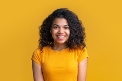 Portrait of young attractive african american woman on bright background. Cute girl with voluminous curly hair looking happy with wide perfect smile on her face.