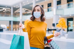 Portrait of casually dressed confident young woman wearing protecting medical mask while walking in mall with bunch of shopping bags in hands. Black friday sales concept.