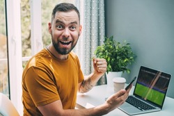 Lucky man celebrating victory after making bets at bookmaker's website. Football fan watching play live broadcast on his laptop computer and  cheering for his favourite team.