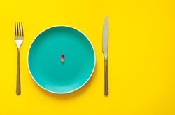 Colorful capsule on plate on yellow background with copy space. Health care or synthetic food concept. Top view. Antipyretic tablet. Coronavirus.