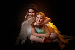 Two teenage girls with white wings in a dark studio with bright flash. Sisters and models posing for a photo shoot like an angel and having fun together