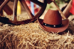 on a haystack the brown cowboy's hat and a wooden wheel lies